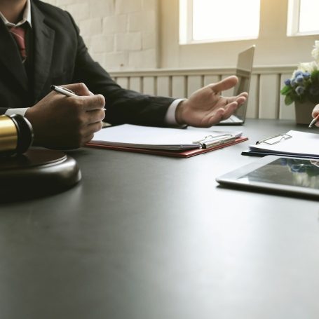 Ein Gerichtstisch mit einem Hammer, Notizen und zwei Händen im Gespräch.